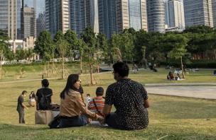 Orang-orang sedang bersantai di taman kota dengan pepohonan rindang.