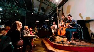 Panggung kecil dengan musisi sedang tampil live di cafe yang ramai.