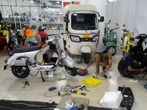 Gambar bengkel yang mengkhususkan diri pada konversi motor listrik, dengan motor listrik yang dipajang dan teknisi sedang bekerja.