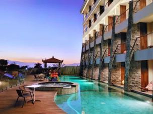 Kolam renang outdoor hotel bintang empat dengan kursi santai di tepi kolam dan beberapa pepohonan.