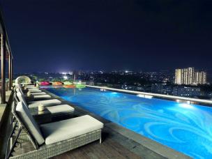 Kolam renang infinity rooftop dengan pemandangan gedung-gedung pencakar langit kota saat malam hari.