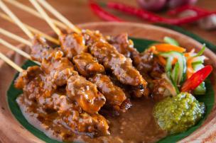 Sepiring sate ayam dengan bumbu kacang melimpah disajikan di warung kaki lima di malam hari.