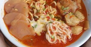 Semangkuk seblak ramen dengan mi ramen, kerupuk, dan topping bakso.