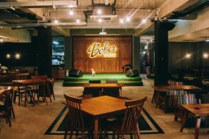 Panggung kecil dengan musisi akustik sedang tampil di cafe yang ramai, pencahayaan temaram.