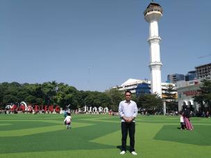 Orang-orang sedang bersantai di rumput sintetis Alun-Alun Bandung dengan latar belakang Masjid Raya.