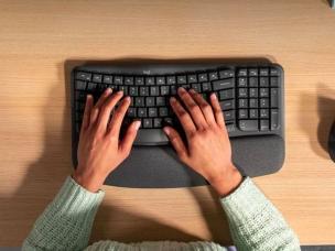 Gambar keyboard ergonomis terpisah dengan sandaran pergelangan tangan berlapis, menunjukkan bagaimana tangan diposisikan secara alami dan nyaman saat mengetik.