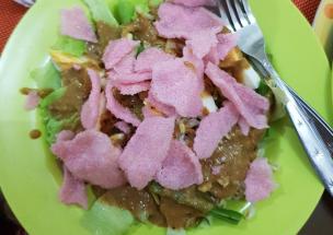 Semangkuk lotek dengan sayuran segar dan potongan lontong di piring.