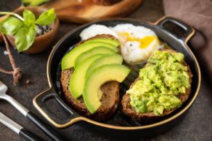 Piring berisi sarapan brunch yang estetik dengan alpukat, telur poached, dan roti panggang di meja kafe.