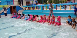 Gambar beberapa anak sedang bermain air di kolam renang umum yang ramai dan ceria.