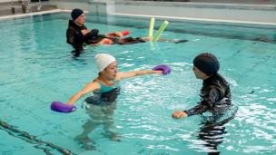Gambar seorang terapis membantu pasien melakukan gerakan terapi di dalam kolam renang air hangat.