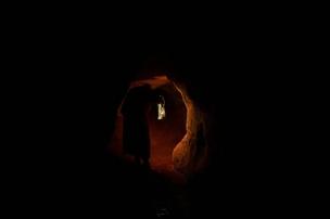 Interior gua yang gelap dan lembab dengan siluet orang memasuki lorong.
