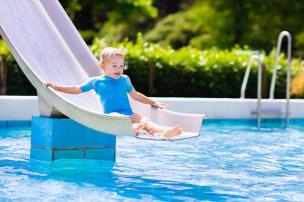 Gambar beberapa anak kecil bermain air di kolam renang dangkal dengan seluncuran mini.
