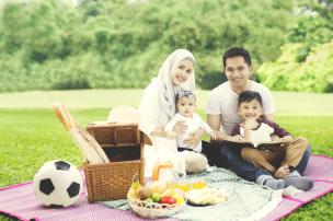 Keluarga sedang piknik di taman dengan anak-anak bermain.