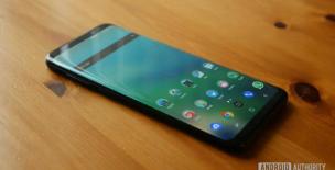 Smartphone futuristik dengan layar melengkung dan efek cahaya holografik, dipegang di atas telapak tangan.