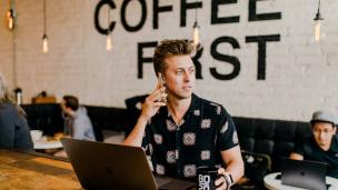 Seseorang sedang bekerja dengan laptop di meja cafe yang modern dan terang.