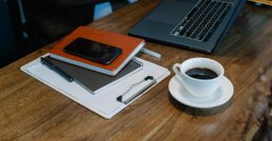 Smartphone elegan diletakkan di samping laptop dan cangkir kopi di meja kerja yang rapi.