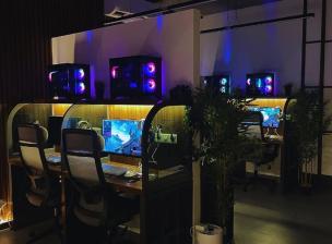 Interior gaming cafe dengan deretan PC gaming spesifikasi tinggi dan kursi ergonomis.