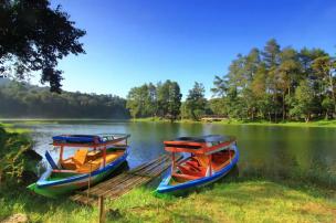 Pemandangan Situ Patenggang dengan perahu dan perbukitan hijau.