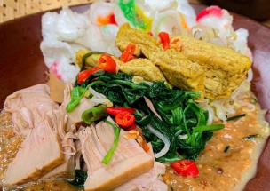 Sepiring lotek dengan sayuran segar dan bumbu kacang yang melimpah disajikan di meja.