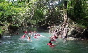 Orang-orang sedang melakukan body rafting di Green Canyon dengan air berwarna hijau toska.