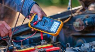 Teknisi sedang memeriksa sistem kelistrikan mobil menggunakan multimeter.