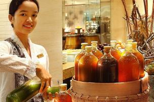 Mbok jamu gendong sedang melayani pembeli, atau gelas berisi aneka jamu tradisional dengan bahan-bahan herbal di sampingnya.