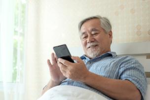 Seorang senior sedang tersenyum sambil menggunakan smartphone yang mudah digenggam.