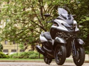 Gambar Yamaha Tricity 155 diparkir dengan elegan di jalan kota modern di Kelapa Gading, menampilkan desain tiga roda yang unik dan daya tarik perkotaannya.