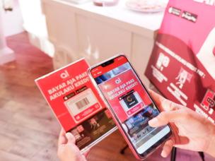  seseorang yang dengan senang hati membuka kotak gadget elektronik yang dibeli dengan Akulaku Paylater, dengan aplikasi Akulaku ditampilkan di smartphone terdekat,