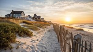 Gambar rumah modern di lereng bukit dengan pemandangan kota saat matahari terbenam.