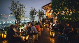 Pemandangan kota Jakarta dari rooftop bar di malam hari dengan lampu-lampu kota.