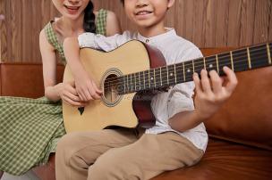 Seorang guru sedang mengajarkan siswa bermain gitar akustik di studio musik.
