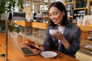 Meja cafe dengan laptop, kopi, dan beberapa orang bekerja dengan tenang.