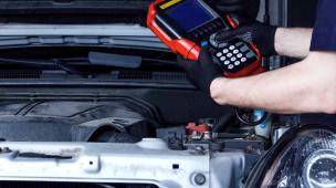 Mekanik sedang melakukan pemeriksaan mesin mobil dengan laptop diagnostik.
