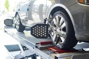 Mobil sedang dalam proses spooring menggunakan alat laser di bengkel yang bersih dan modern.