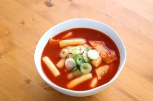 Semangkuk tteokbokki dengan kuah seblak merah dan topping.