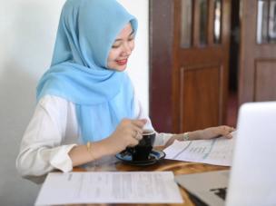 Gambar seseorang yang diam-diam membaca syarat keuangan di tablet, dengan elemen atau pola arsitektur Islam samar di latar belakang, dan logo Alami Sharia terlihat jelas