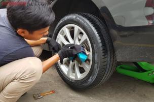 Ban mobil baru sedang dipasang pada velg oleh seorang mekanik di bengkel ban.