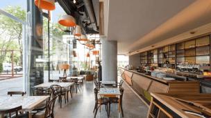 Interior coffee shop yang estetik dengan pencahayaan alami yang masuk melalui jendela besar, terlihat beberapa spot duduk yang nyaman.