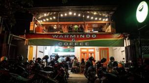 Suasana Warmindo yang ramai dengan anak muda sedang menikmati mie instan dan minuman.