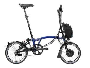 Gambar sepeda Brompton Bicycle terlipat berdiri dengan elegan di lobi kantor modern atau kafe, menonjolkan daya tarik perkotaan yang canggih, dengan latar belakang samar SCBD Jakarta Pusat.