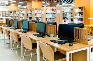 Gambar perpustakaan sekolah modern dengan meja belajar individual dan komputer yang bersih.