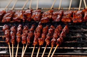 Tusuk sate maranggi sedang dibakar di atas bara arang dengan asap mengepul.