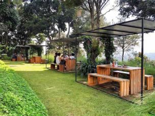 Area outdoor cafe dengan meja dan kursi yang nyaman, menghadap ke pemandangan danau atau perbukitan hijau.