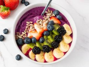 Semangkuk smoothie bowl dengan topping buah segar dan granola di meja kayu.