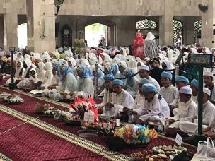 Gambar siswa-siswi mengenakan seragam sekolah muslim sedang membaca Al-Quran di masjid sekolah.