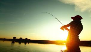 Orang sedang memancing di kolam dengan latar belakang saung dan piring berisi ikan bakar tersaji di meja.