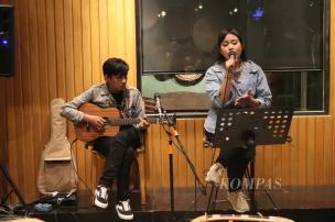 Seorang musisi sedang bermain gitar akustik di panggung kecil sebuah kafe.