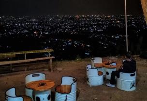Pasangan duduk di kafe rooftop dengan pemandangan city light Bandung di malam hari.