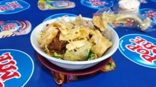 Semangkuk mie ayam bakso hangat disajikan di meja warung kaki lima di malam hari.